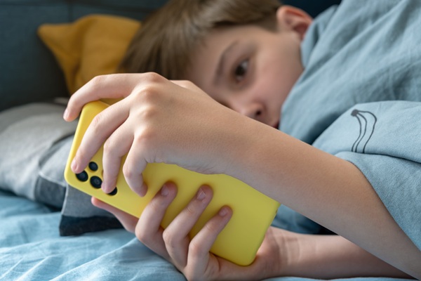 Ein Kind, das spät abends im Bett liegt und ein Smartphone benutzt